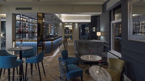 A modern bar area with a long counter, bar stools, and a seating area with chairs and a round table. - Clifton Arms Hotel (Lytham St. Anne's)