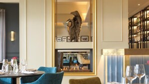 A dining area with round tables and chairs, a fireplace with framed pictures above, and a bookshelf with various items. - Clifton Arms Hotel (Lytham St. Anne's)