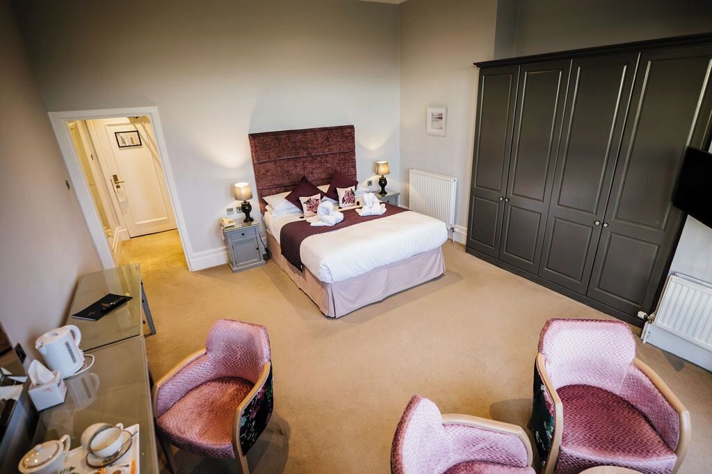 A hotel room with a bed, bedside tables, a wardrobe, and two armchairs.