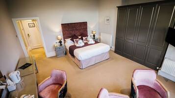 A hotel room with a bed, bedside tables, a wardrobe, and two armchairs.