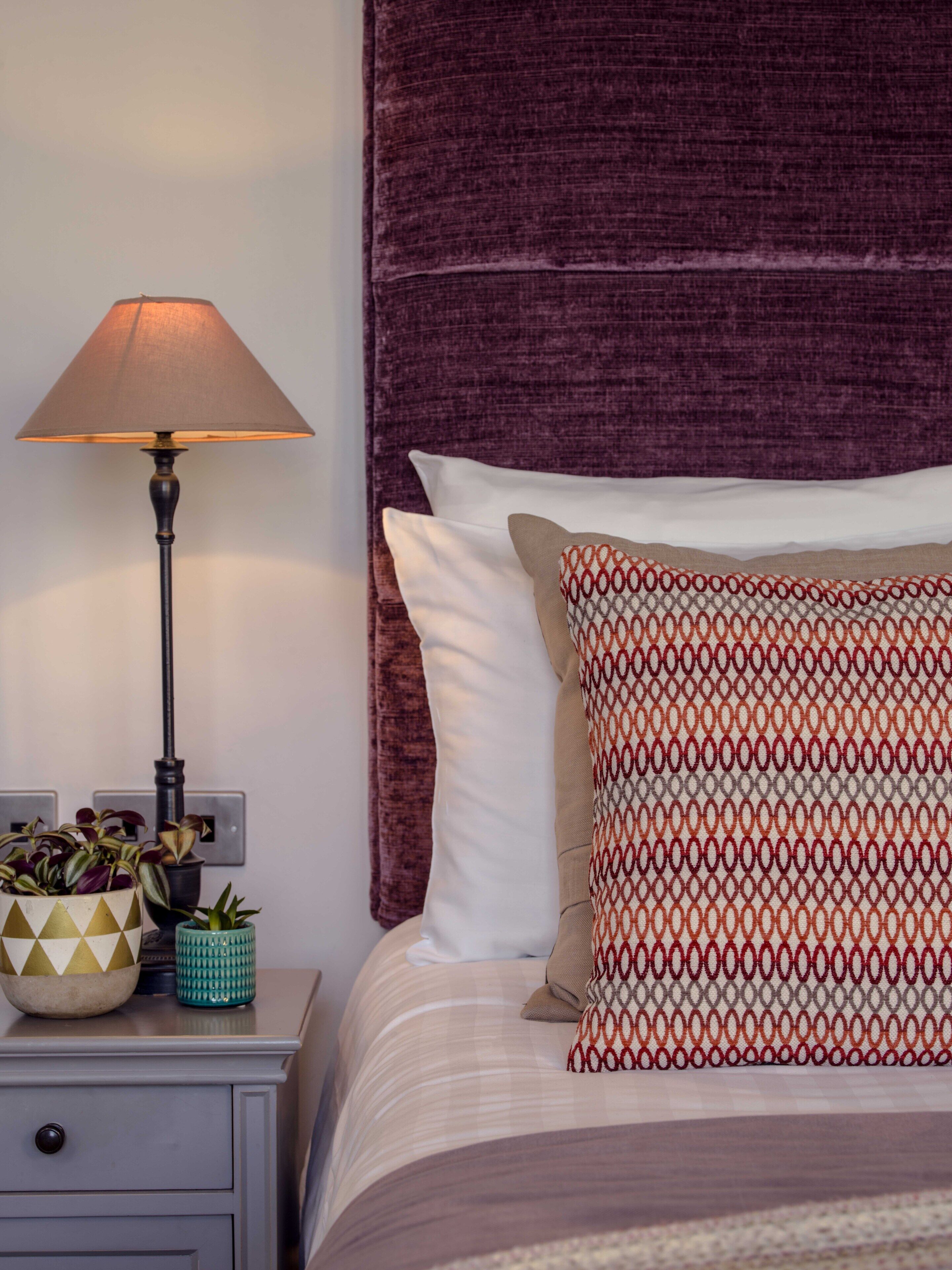 A neatly made bed with a patterned pillow and a plain pillow, a bedside lamp, and a nightstand with decorative items.