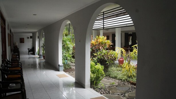 Un pasillo con techos abovedados, suelo de baldosas y un jardín con diversas plantas y un pequeño elemento acuático.