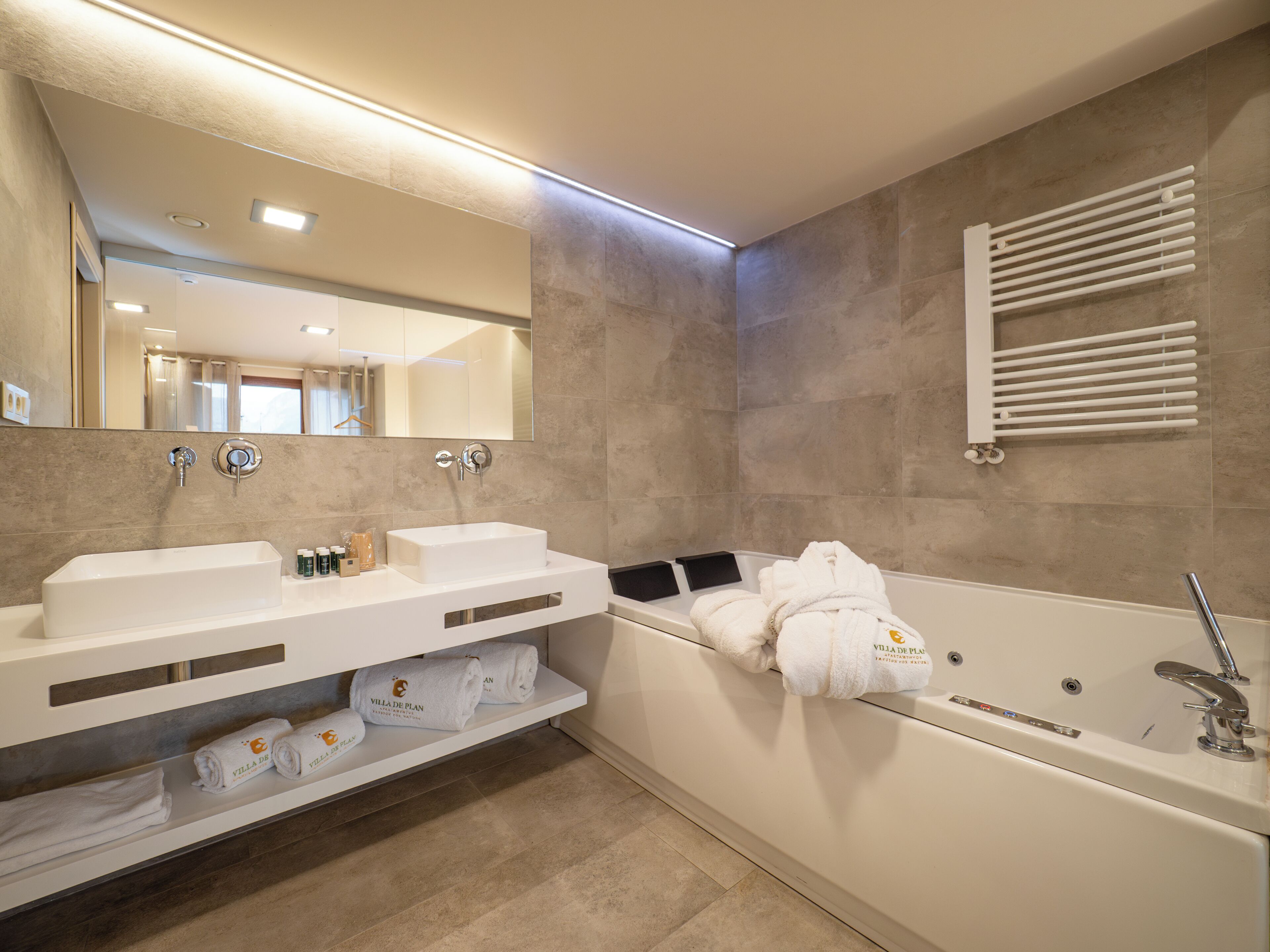 Une salle de bain moderne avec une grande baignoire, deux lavabos, un porte-serviettes et un miroir.