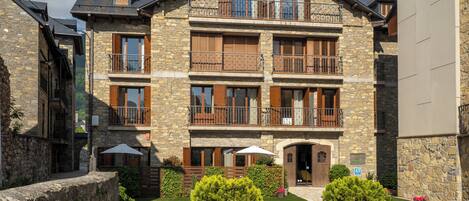 A multi-story stone building with balconies, a well-maintained lawn, and potted plants.