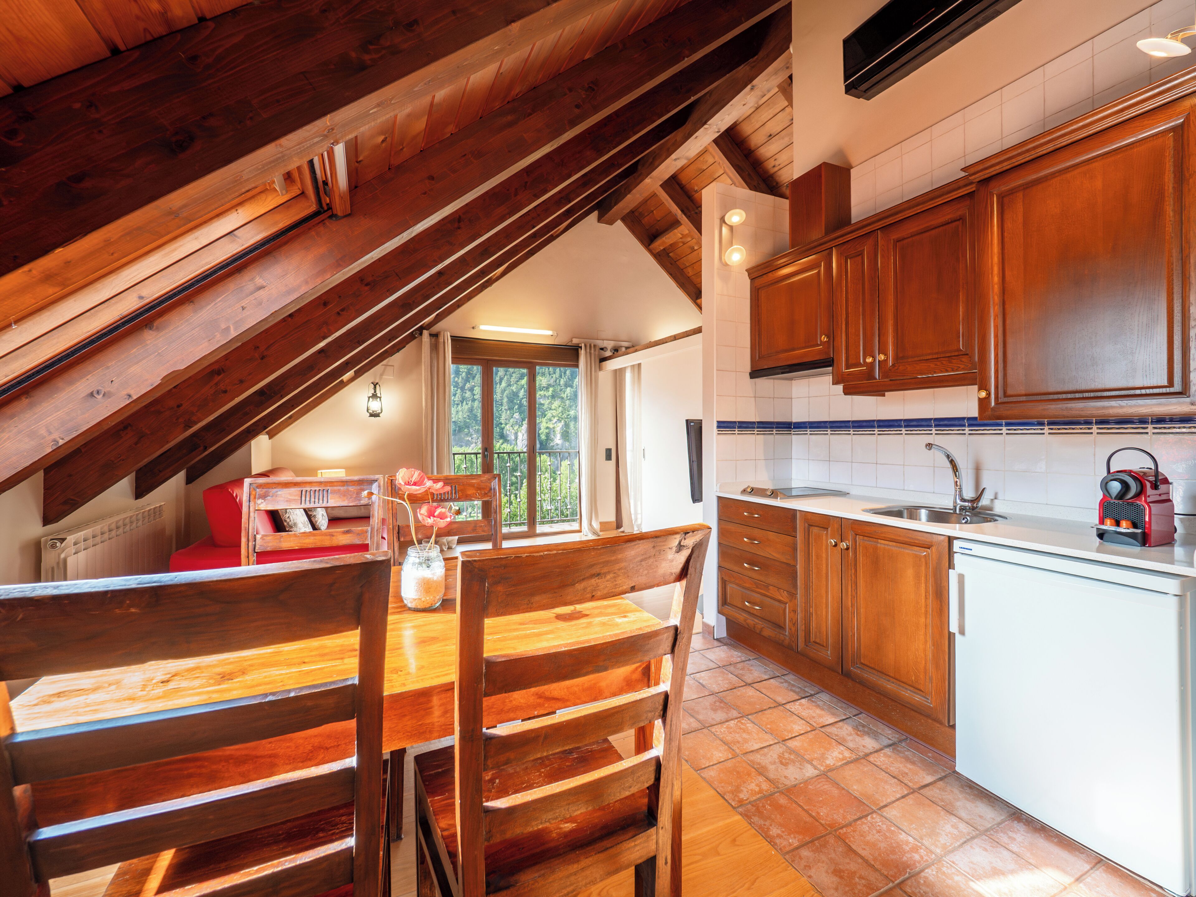 A kitchen with wooden cabinets, a dining table with chairs, and a view of the outdoors through a window.