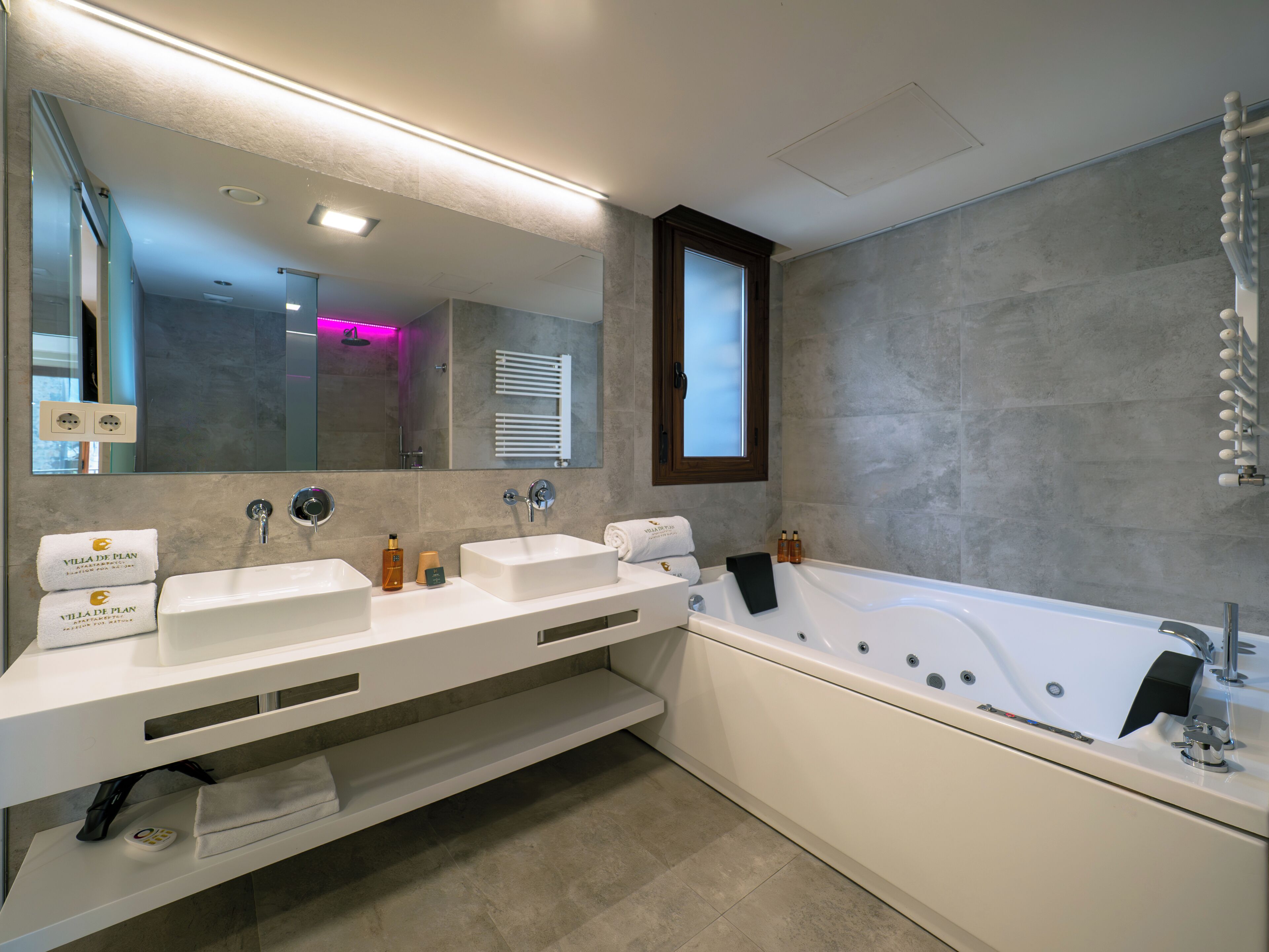 A modern bathroom with two sinks, a bathtub, a large mirror, and a window.