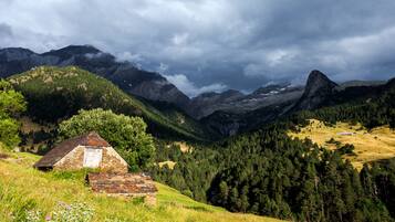 A rustic stone house with a sloped roof, surrounded by lush green hills and dense forests.
