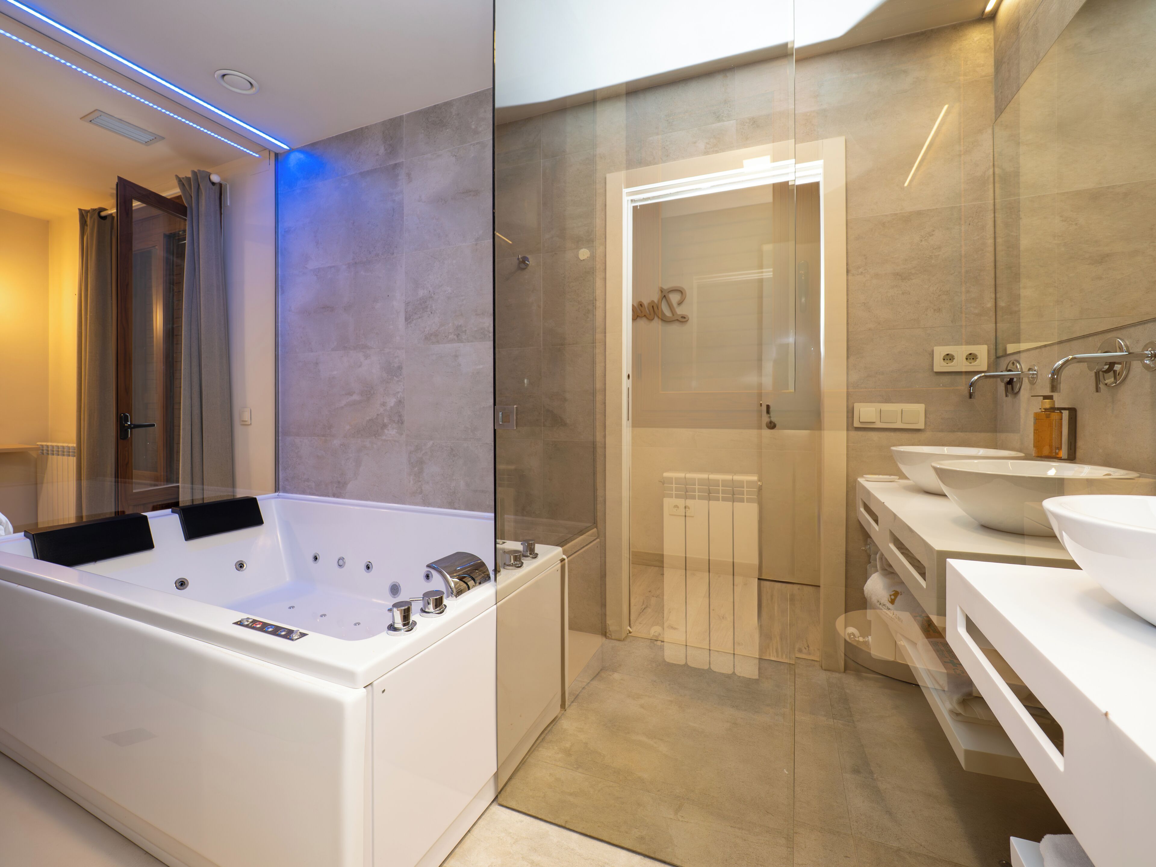A modern bathroom with a large bathtub, two sinks, and a glass shower enclosure.