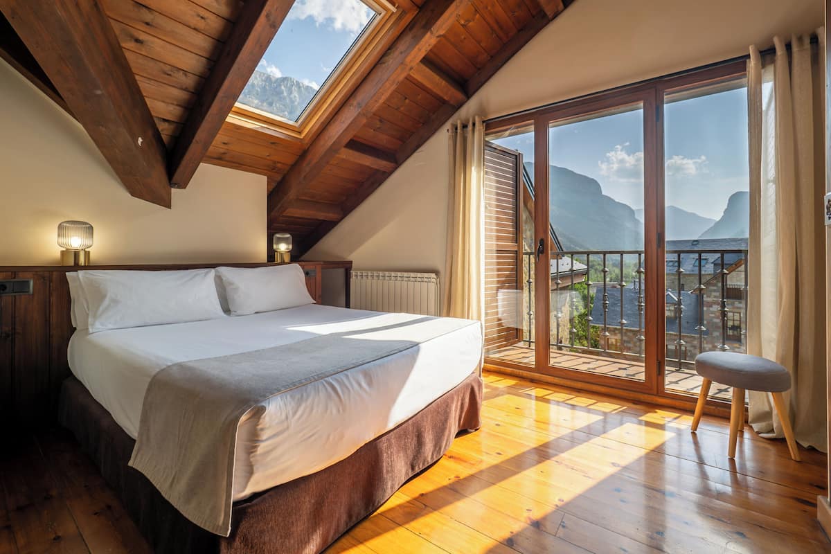 A bedroom with a bed, a nightstand, a lamp, and a view of a balcony with a railing.