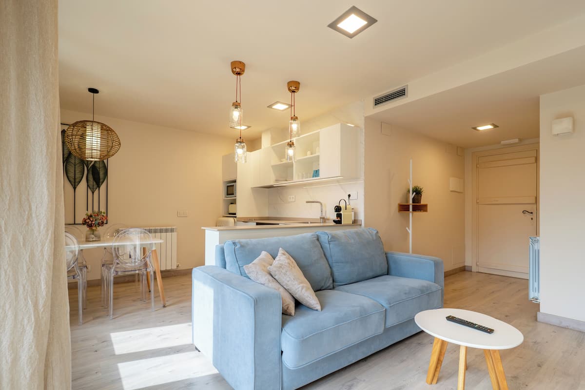 A modern living room with a sofa, a dining table with chairs, a kitchen area, and a door.
