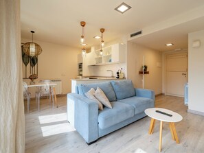A modern living room with a sofa, a dining table with chairs, a kitchen area, and a door. - Apartamentos Villa de Plan (Plan)