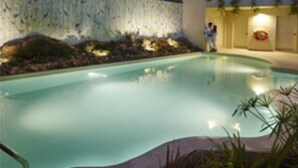 Una piscina con un muro de piedra y plantas, rodeada por un edificio moderno con una lámpara.