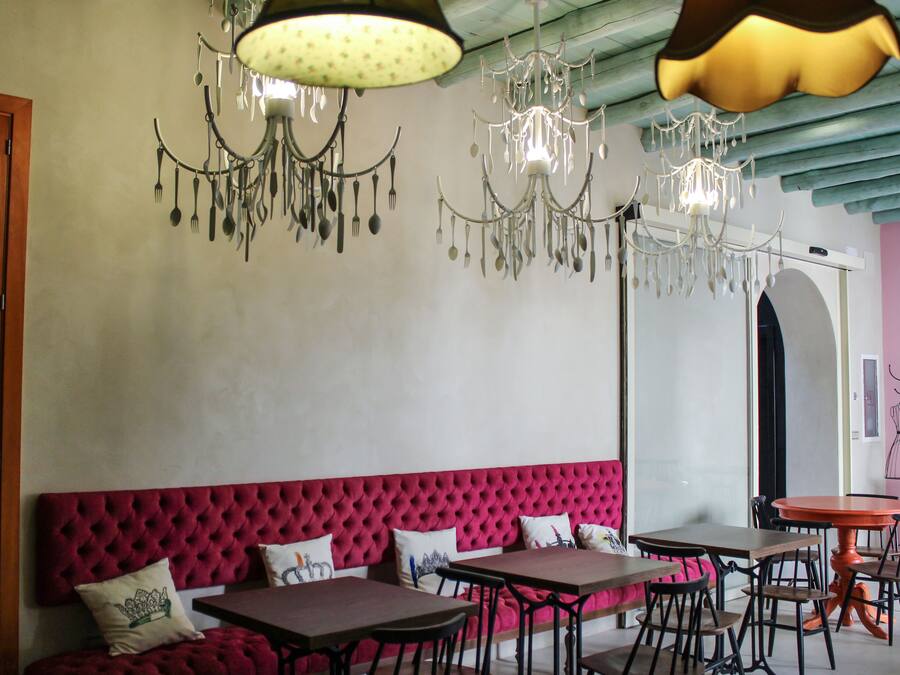 Un comedor con un banco tapizado rojo, varias mesas y candelabros con utensilios colgantes.