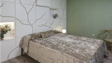 Un dormitorio con cama, una pared con diseño de rama de árbol, una silla y una pequeña mesa con una planta.
