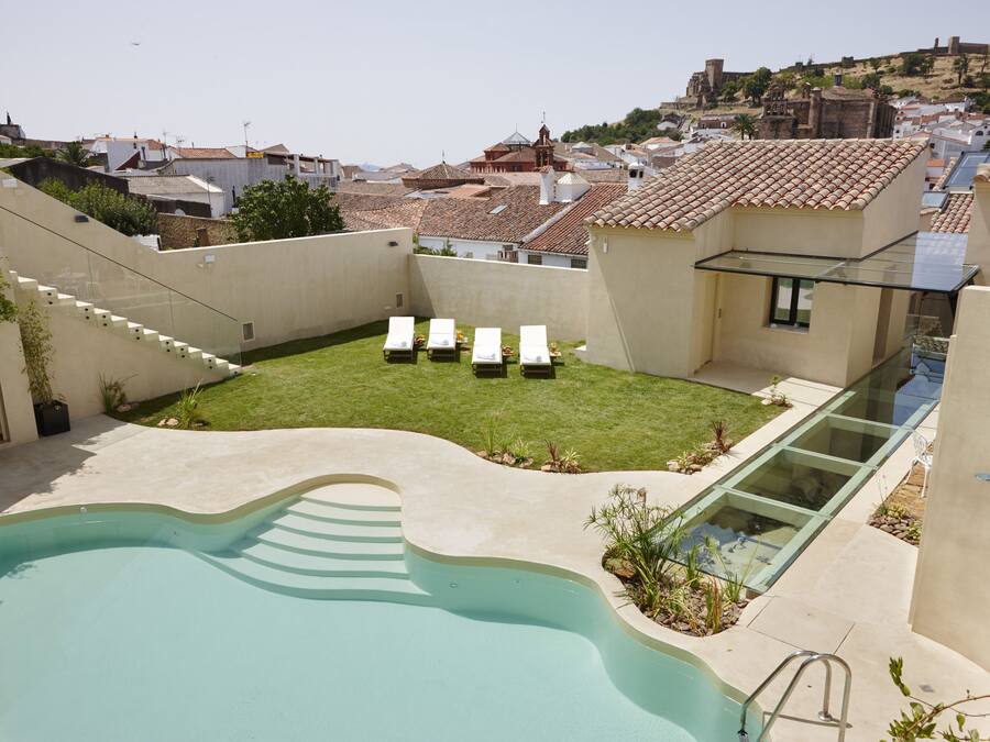 A swimming pool with a glass-enclosed deck, a grassy area with lounge chairs, and a view of a historic hilltop in the background.