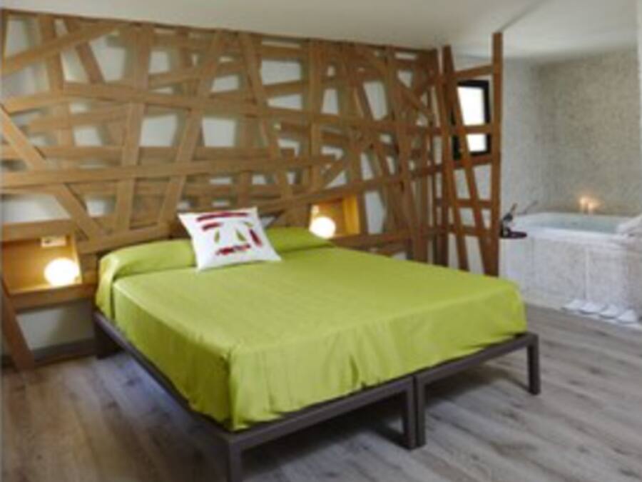 A bedroom with a wooden headboard, a bed with a green bedspread, bedside lamps, and a small table with a lamp.