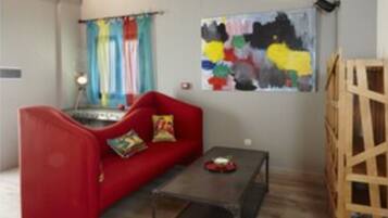 Une pièce avec un canapé rouge, une petite table, une échelle en bois et un tableau abstrait aux couleurs vives accroché au mur.