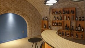 Una zona de bar con pared de ladrillo, estanterías llenas de botellas y taburetes.