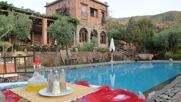 Zona de piscina con un edificio de piedra al fondo, mobiliario exterior y una mesa con saleros y pimenteros.