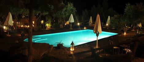 Ein Schwimmbadbereich bei Nacht mit Liegestühlen und Sonnenschirmen.