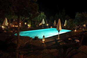 A nighttime swimming pool area with lounge chairs and umbrellas.