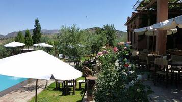 An outdoor dining area with tables and chairs, umbrellas, and a pool.