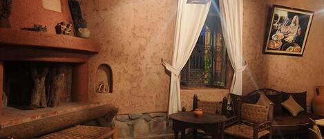 Una habitación acogedora con chimenea, pared de piedra, banca de madera, mesa con sillas y un cuadro en la pared.