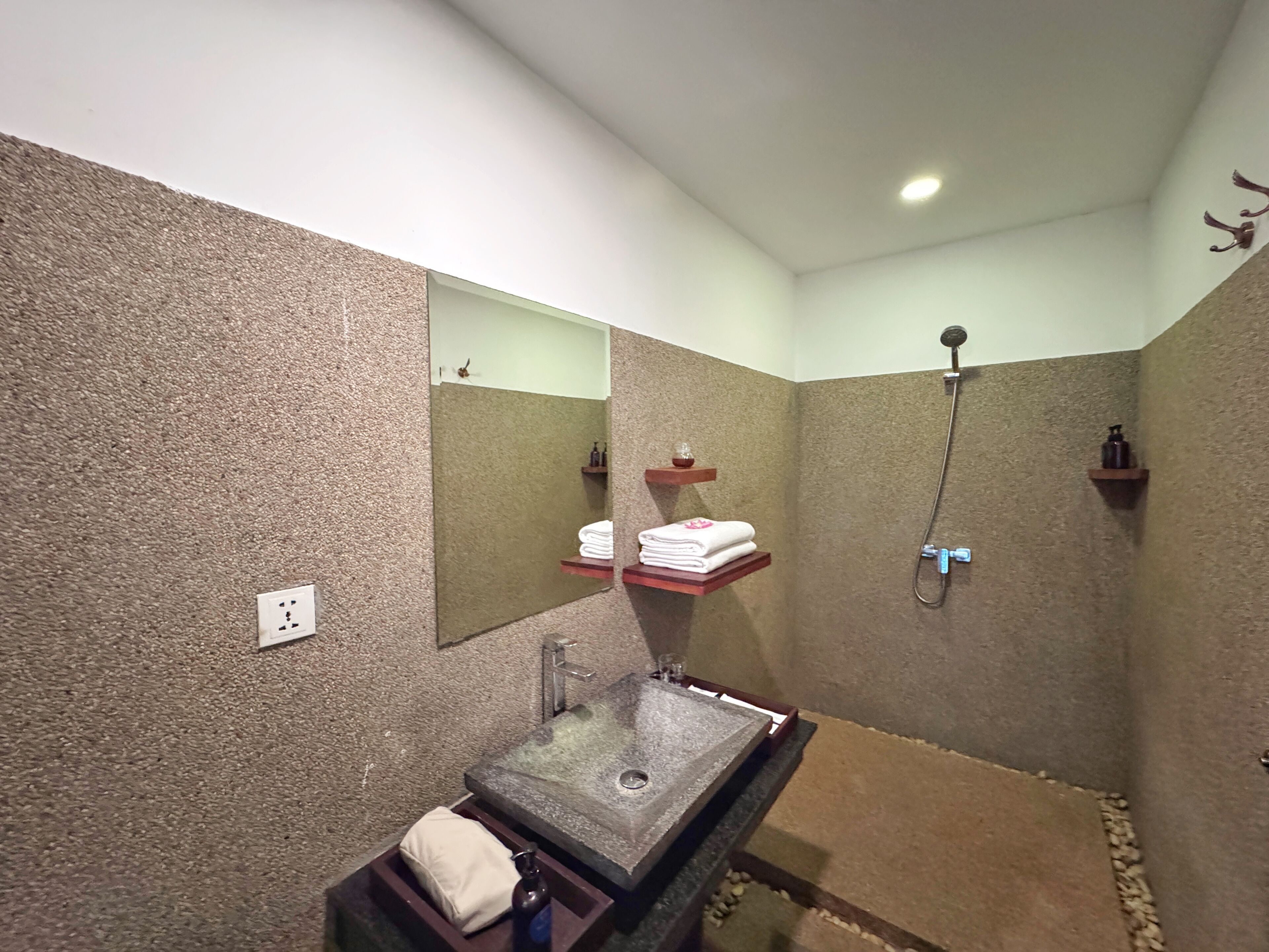 A bathroom with a stone sink, a mirror, a shower, and shelves with towels.