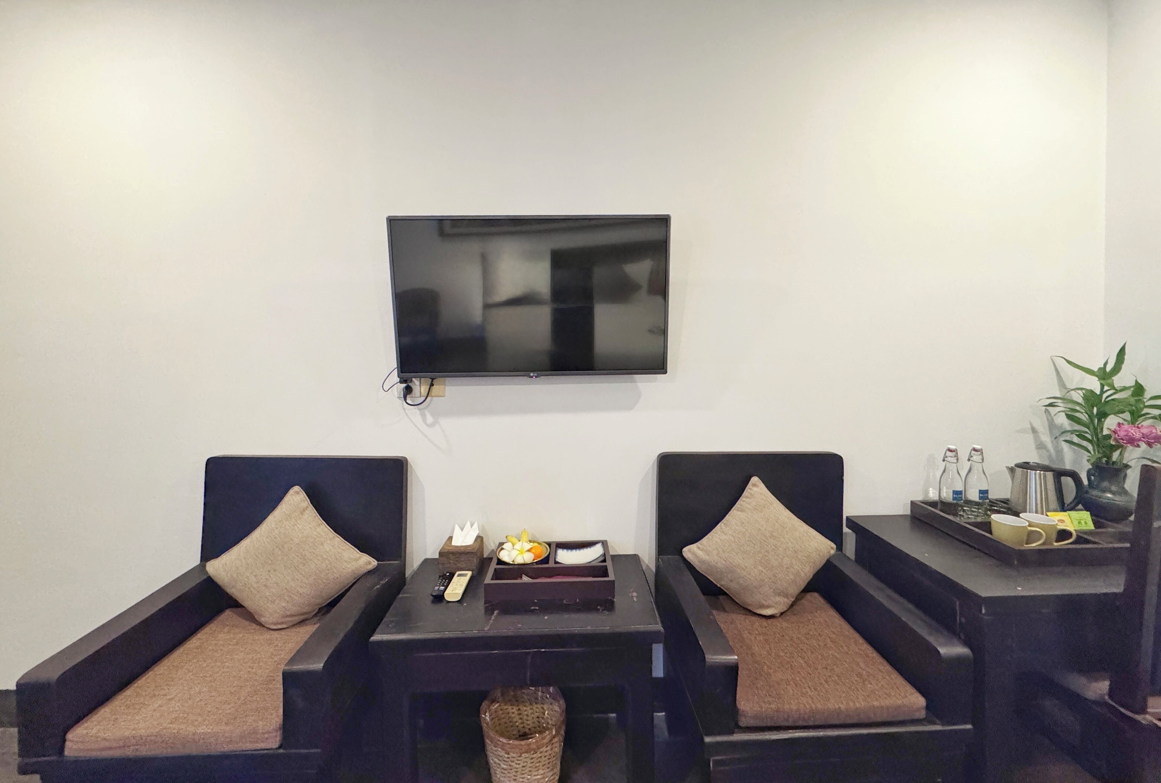 Une pièce moderne avec deux canapés sombres, une petite table avec une télécommande, un plateau contenant des objets décoratifs et un téléviseur fixé au mur.