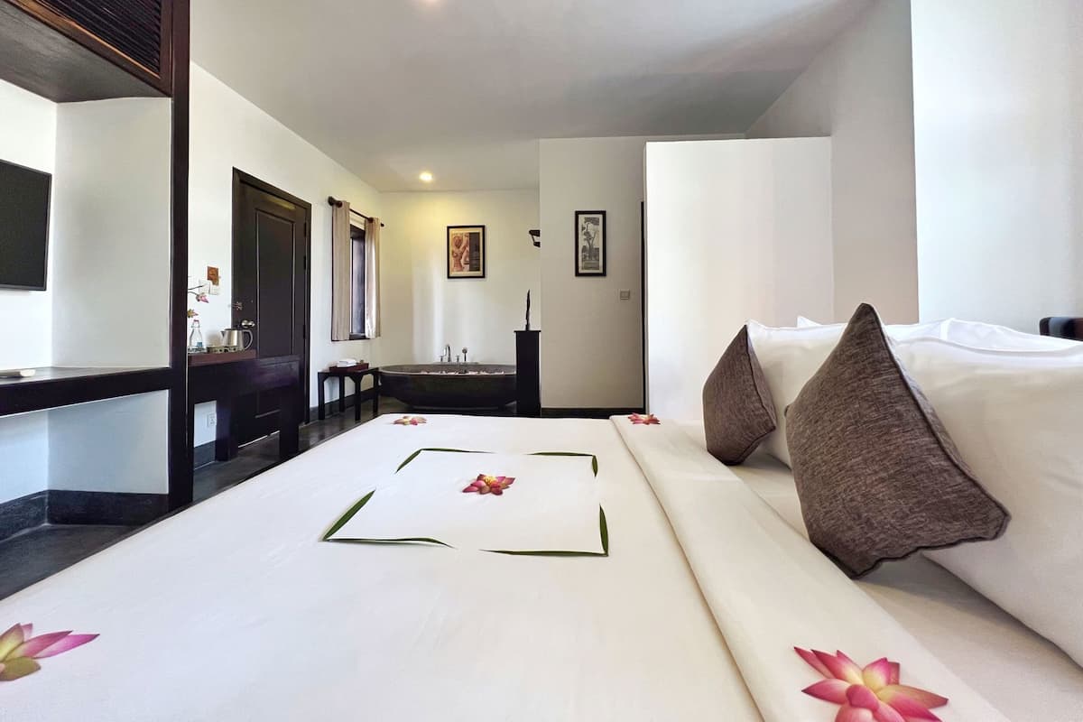 A hotel room with a bed, a desk, a chair, a bathtub, and a mirror.