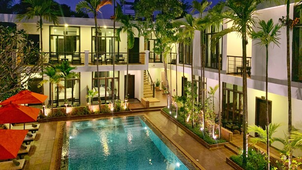 A multi-story hotel with a swimming pool, outdoor seating, and palm trees. - The Bliss Angkor (Siem Reap)