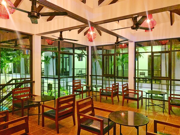 A spacious indoor area with wooden furniture, large windows, and ceiling fans.