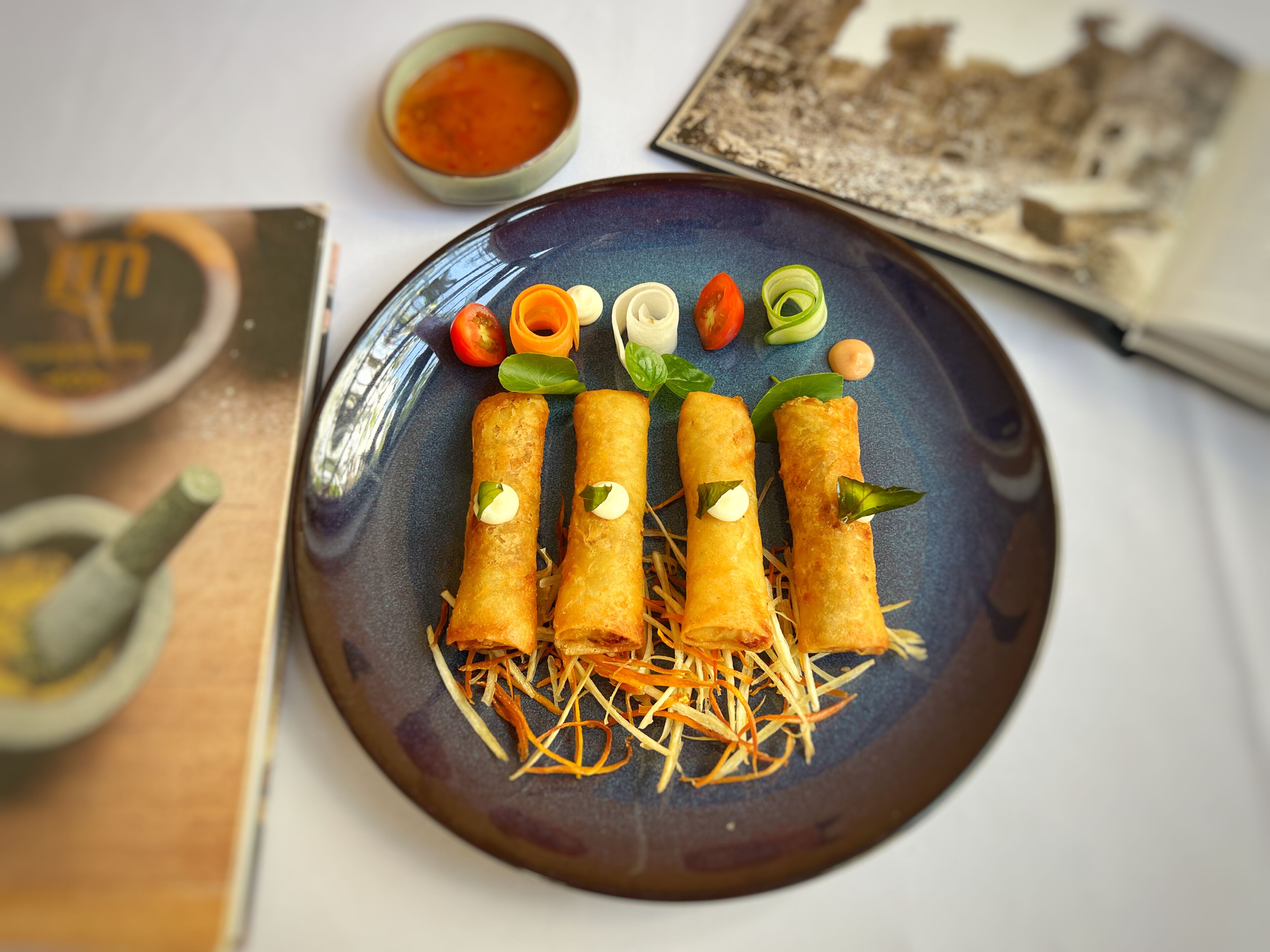A plate of spring rolls garnished with vegetables and a small bowl of sauce.