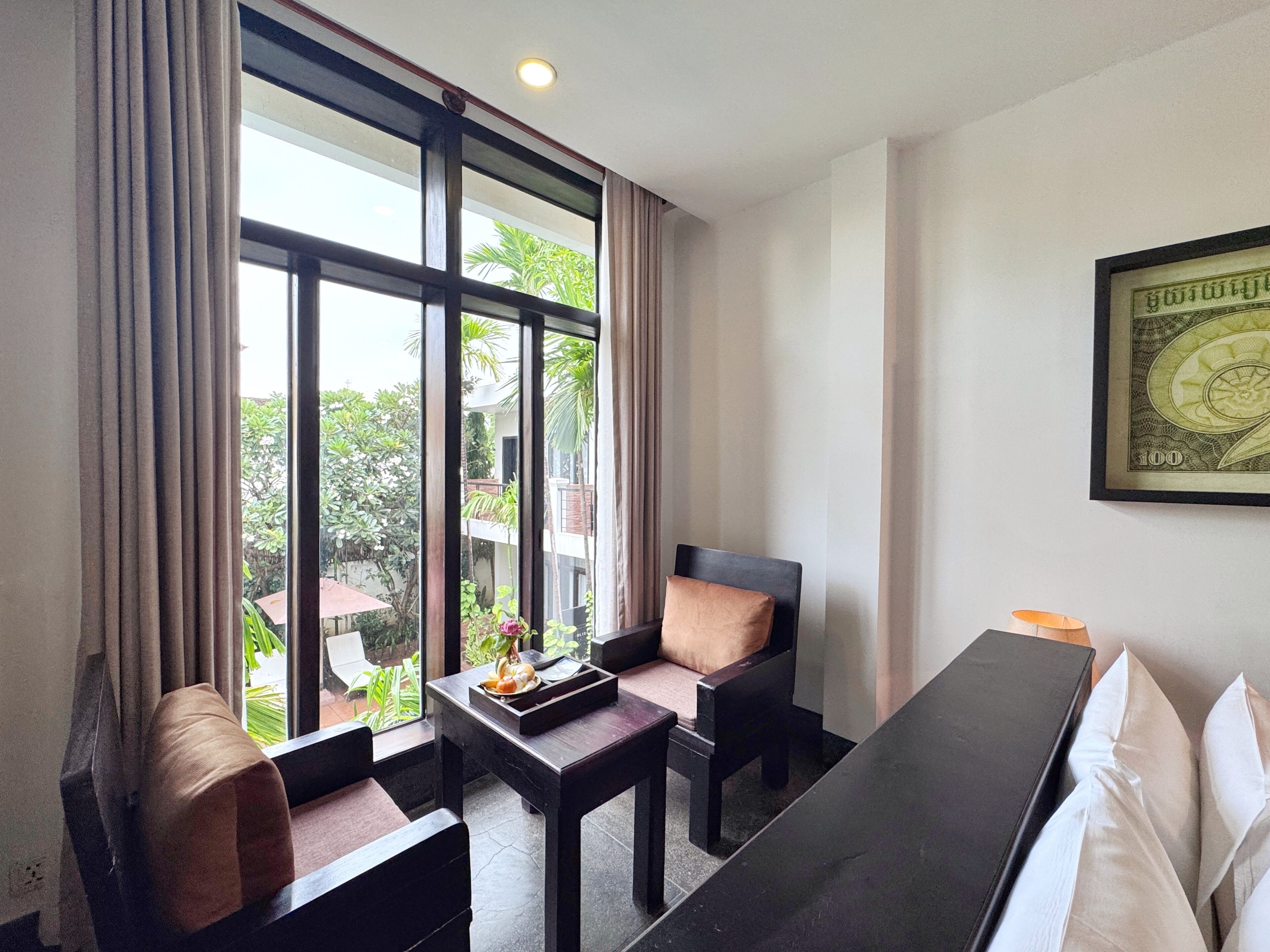A hotel room with a large window, a sofa, a small table with a tray, and a framed picture on the wall.
