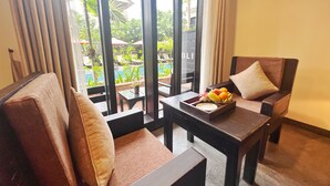 A room with two cushioned chairs, a small table with a fruit bowl, and a view of a pool and greenery outside. - The Bliss Angkor (Siem Reap)