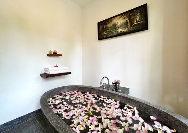Un baño con una bañera independiente llena de pétalos de rosa, un perchero con toallas dobladas y un cuadro enmarcado en la pared.