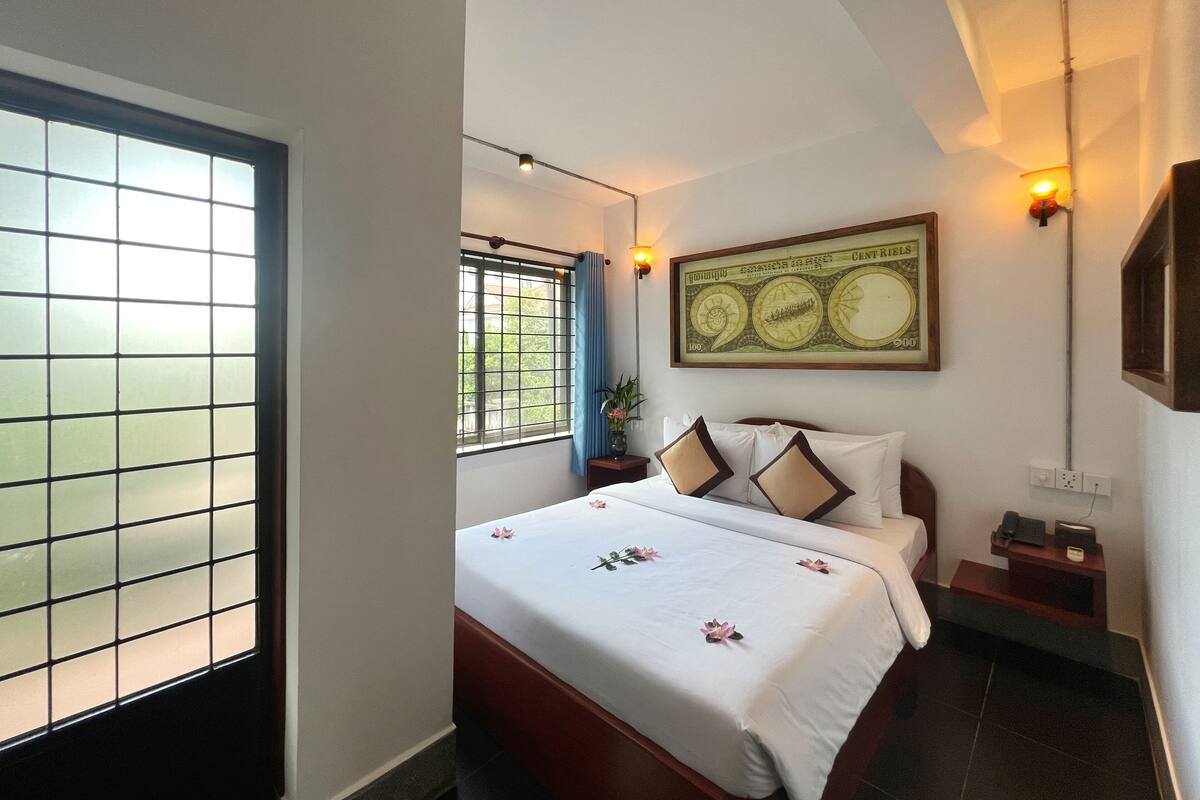 A hotel room with a bed, a window with a view, a wall-mounted picture, and a bedside table with a lamp.