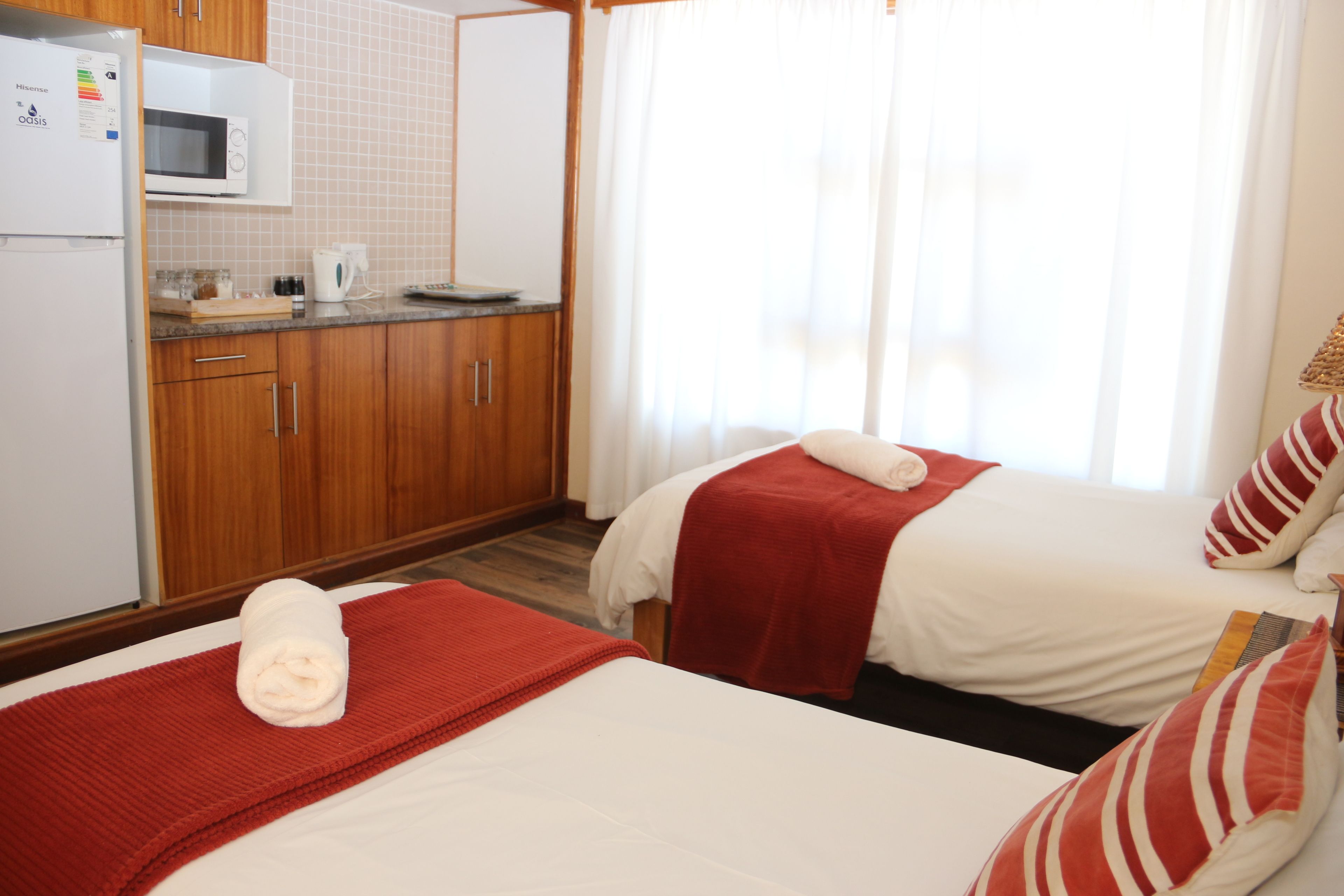 A hotel room with two beds, a kitchenette, and a window with curtains.