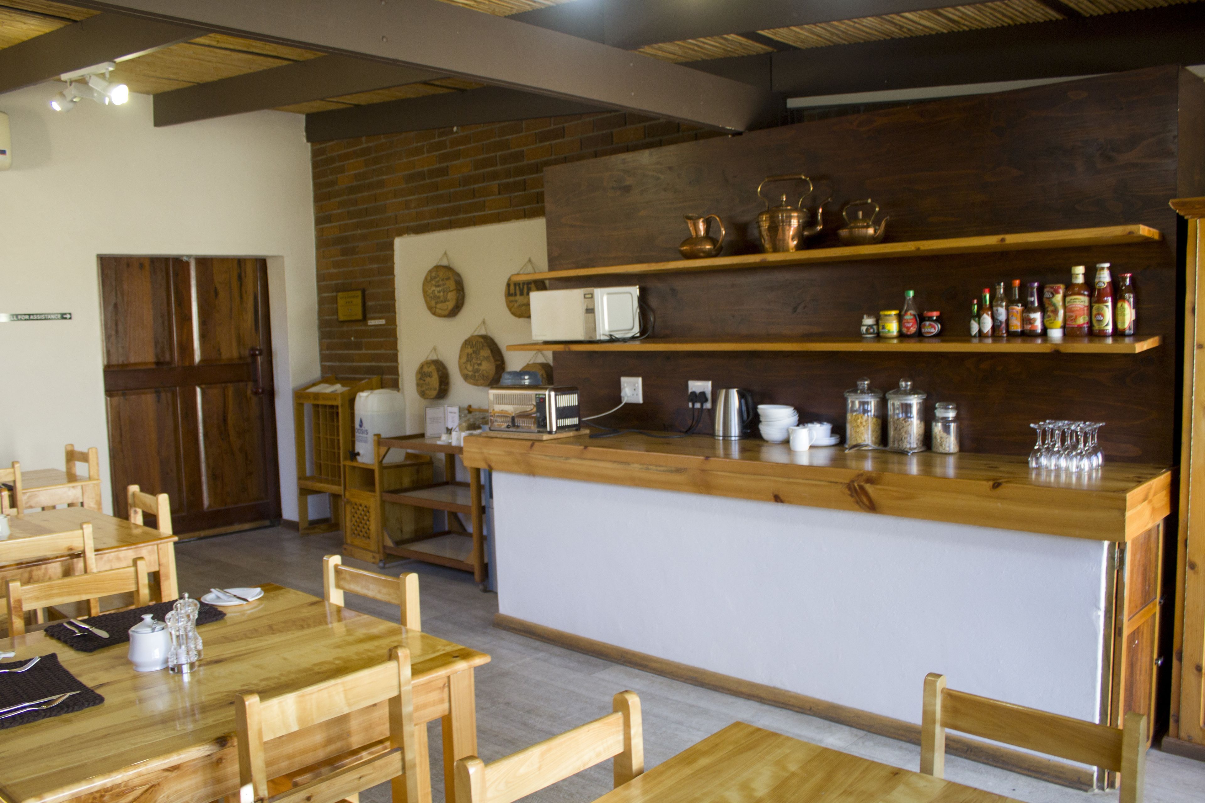 A restaurant with wooden tables and chairs, a central bar area with shelves of condiments, and a brick wall.