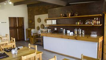 A restaurant with wooden tables and chairs, a central bar area with shelves of condiments, and a brick wall.