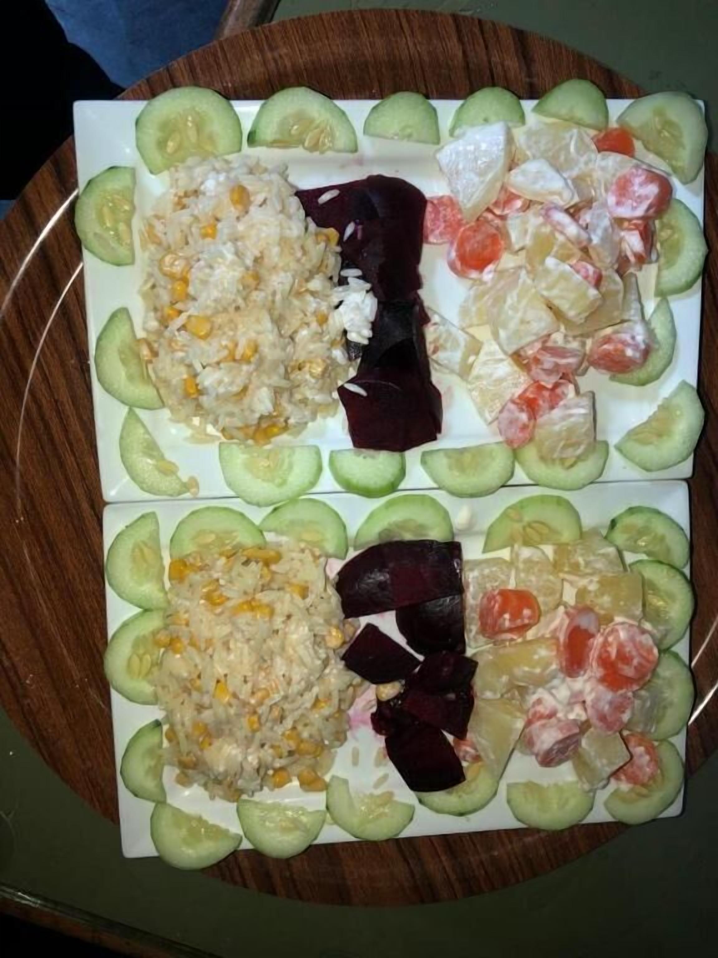 A plate with various food items including rice, beets, and tomatoes, surrounded by cucumber slices.