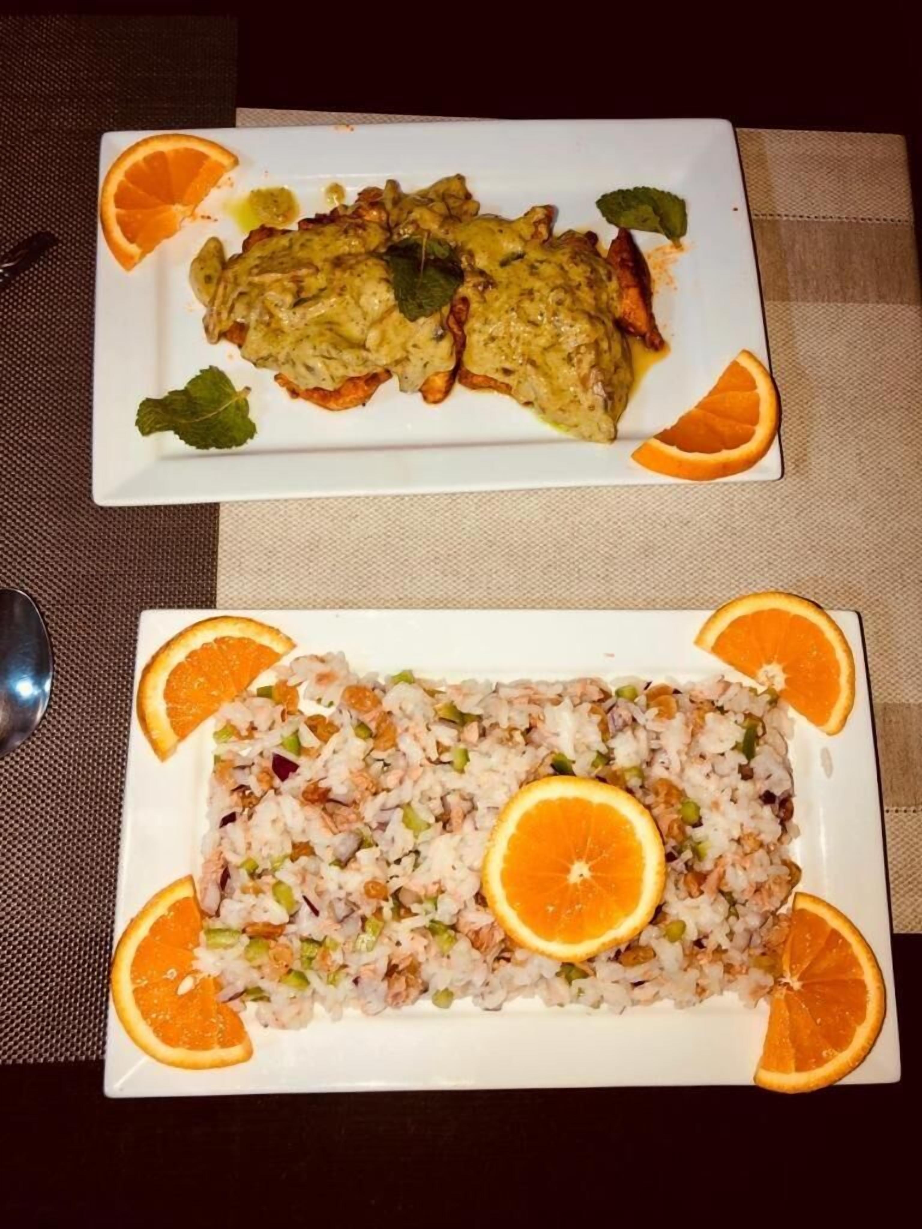Two rectangular white plates with food, garnished with orange slices and mint leaves.