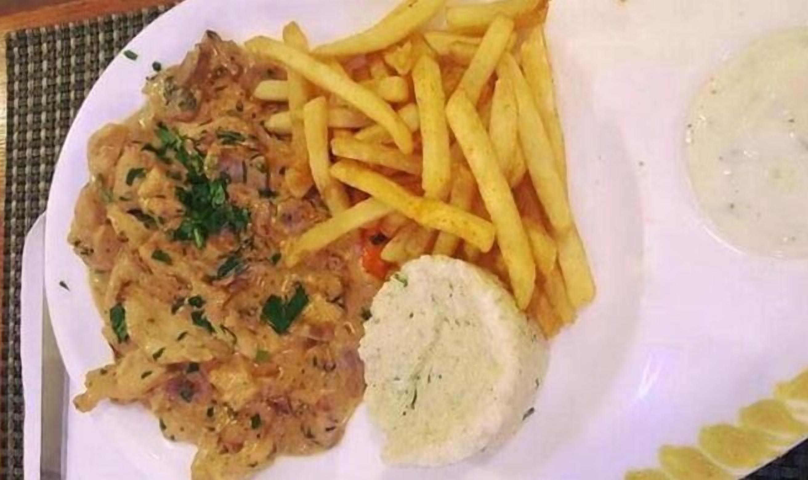 Een bord met een vleesgerecht, friet en een portie saus.