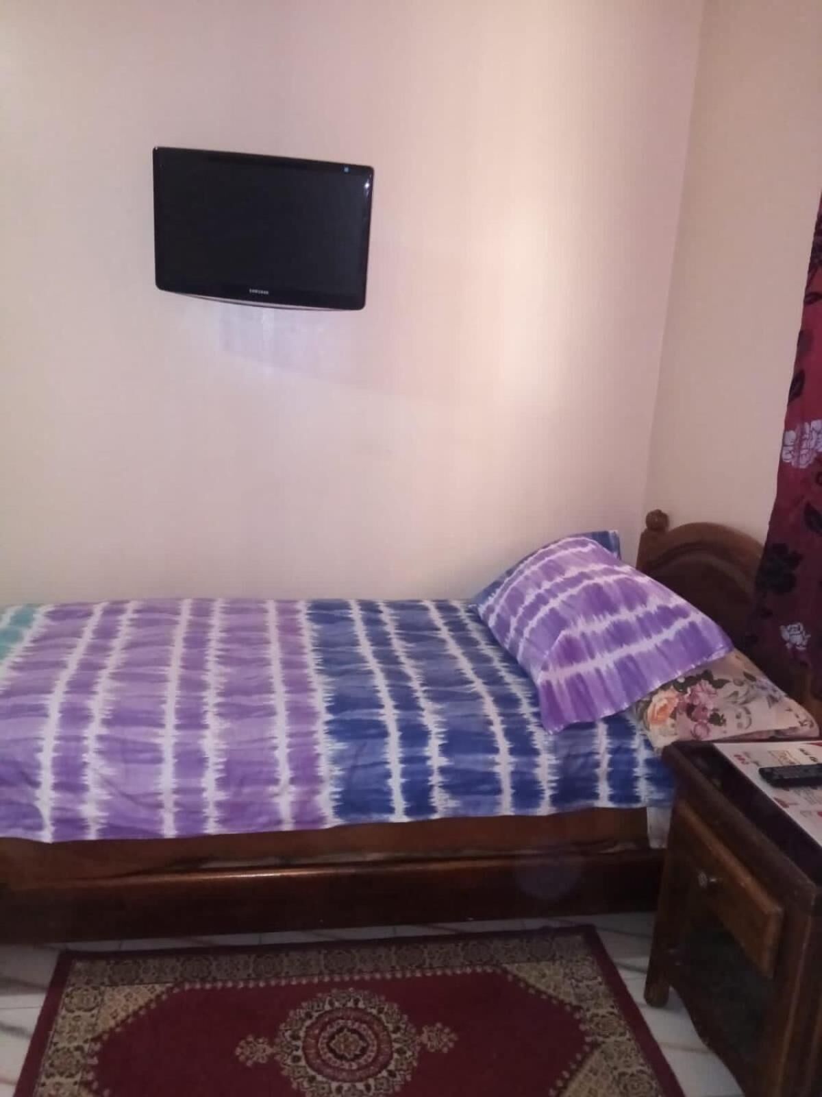 A bedroom with a bed, a television mounted on the wall, and a small wooden table beside the bed.