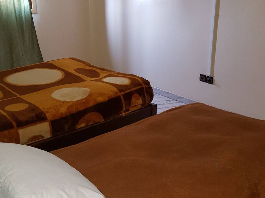 A bedroom with a bed, a TV mounted on the wall, and a window with curtains.