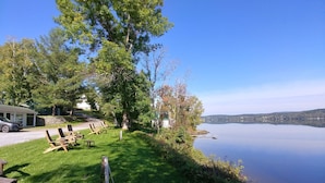 Una propiedad frente al lago con un área de césped, sillones de madera y vistas al lago.