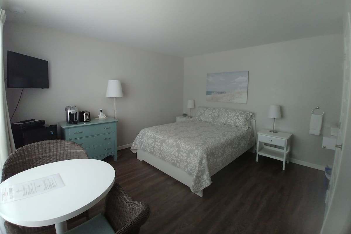 A hotel room with a bed, a desk, a chair, a television, and a painting on the wall.