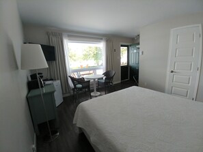 A hotel room with a bed, a desk with a lamp, a chair, a small table, and a window with curtains. - Auberge Marie Blanc (Temiscouata-sur-le-Lac)