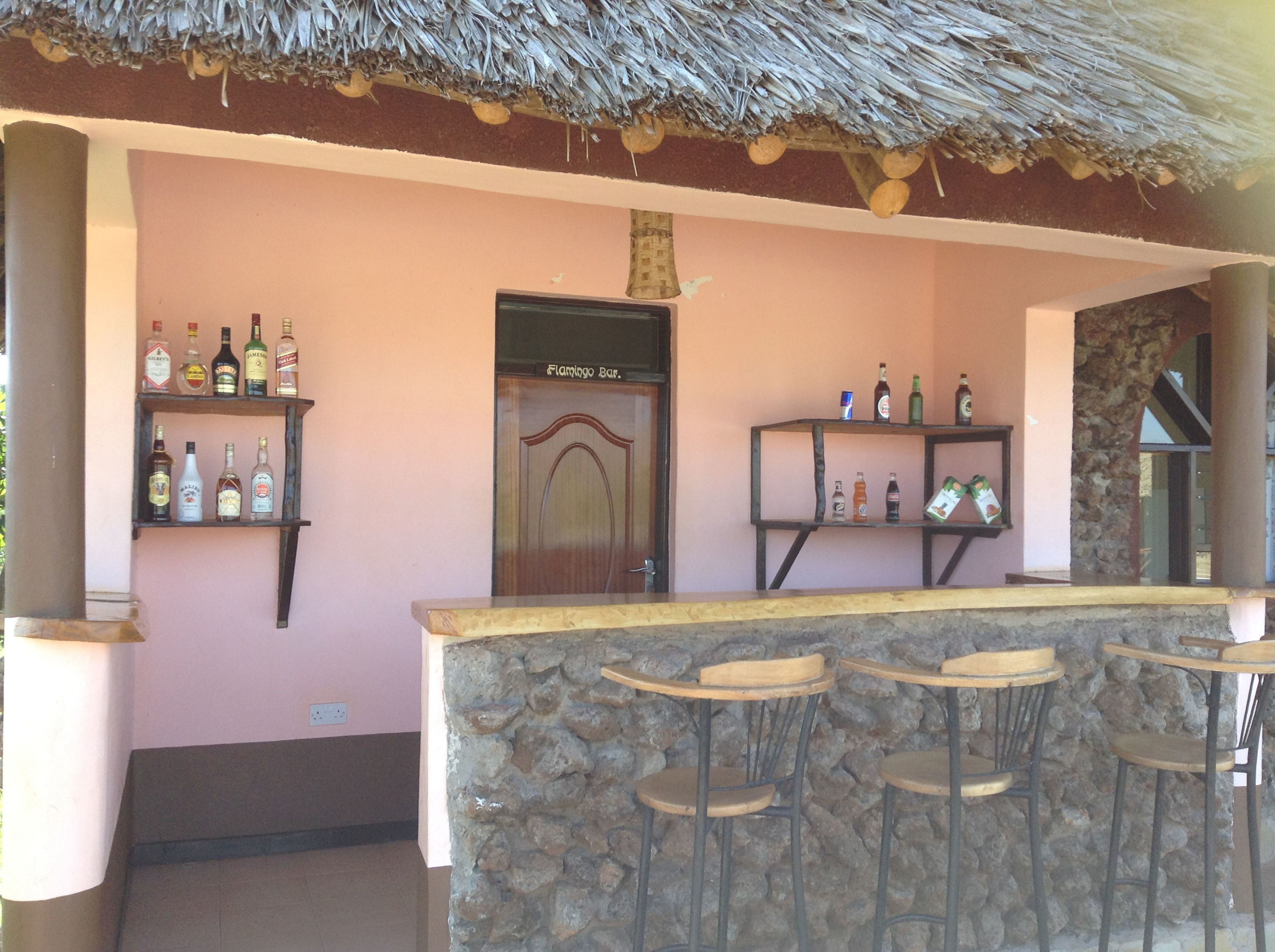 A bar area with a stone counter and wooden stools, shelves with bottles, and a door labeled "Flamingo Bar."