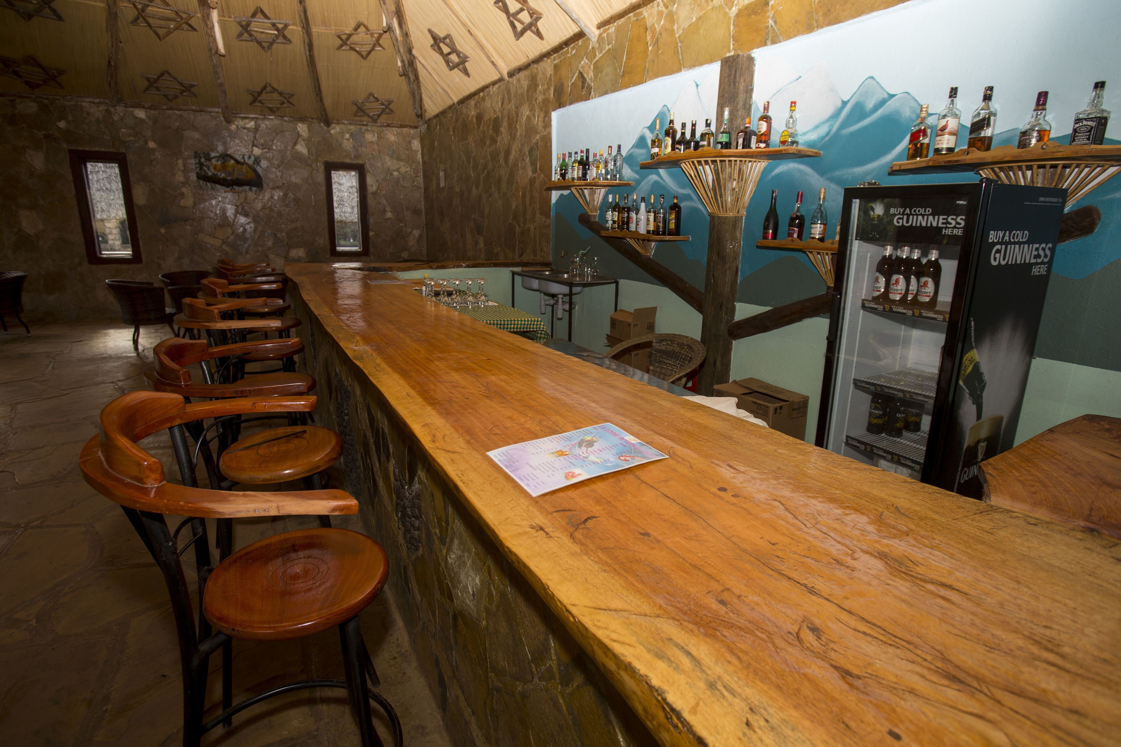 A bar area with wooden chairs, a wooden counter, and shelves with bottles.